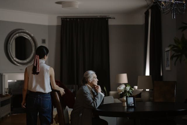 An Elderly Woman Sitting on Wooden Chair Beside the Table